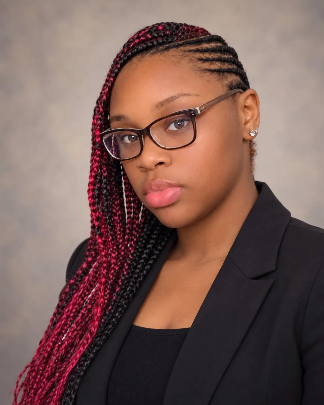 Gigi, founder of Gigi Promotions, wearing glasses and a black blazer with burgundy braids.